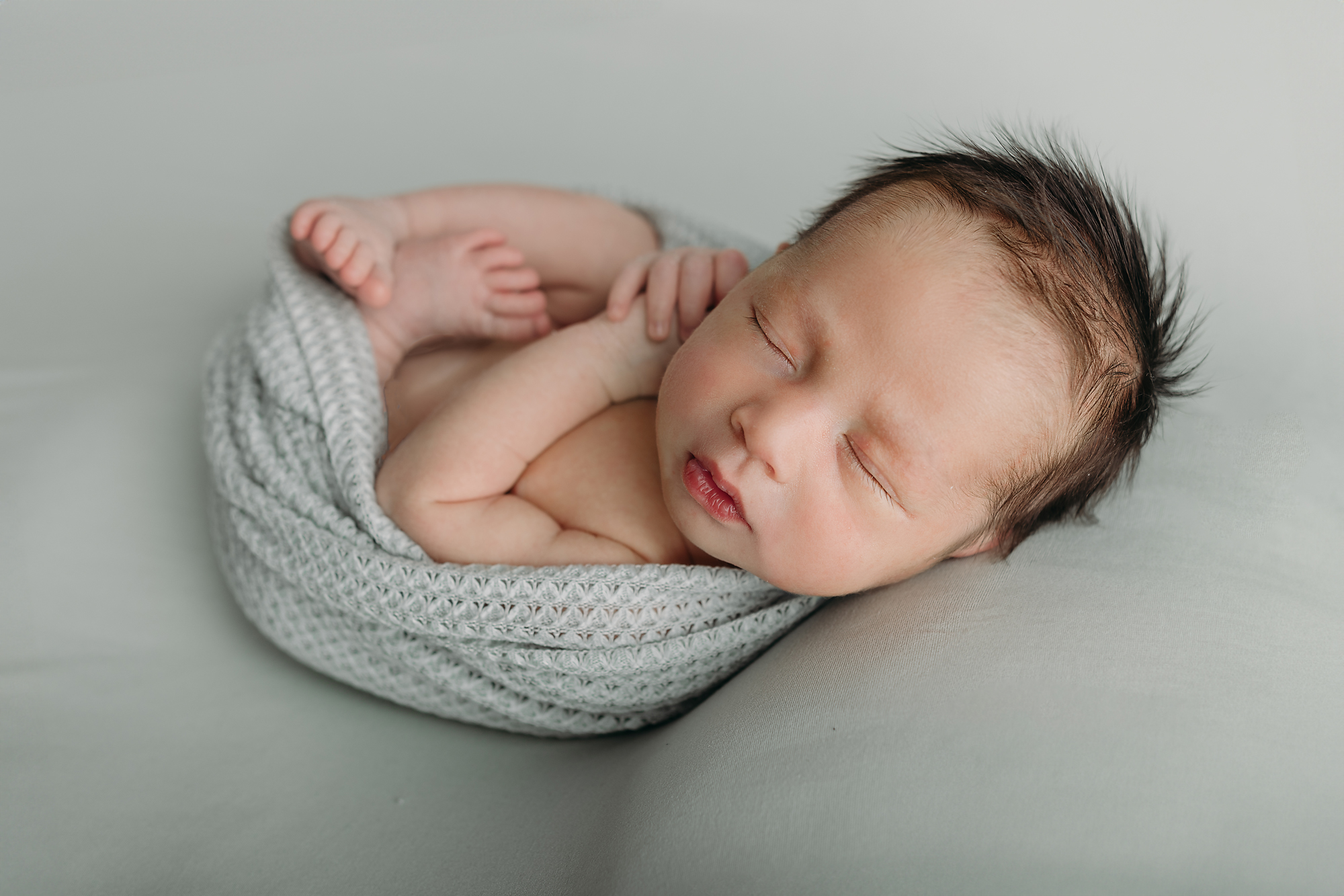 newborn baby boy swaddled in sage sleeps peacefully 