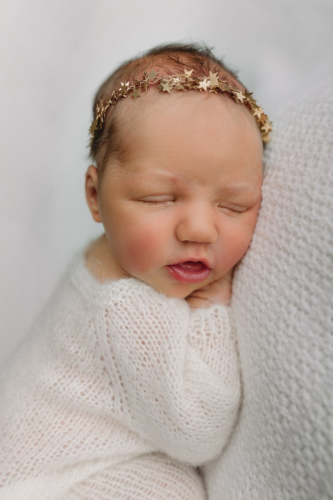 A sleeping newborn wrapped in a soft white knit blanket