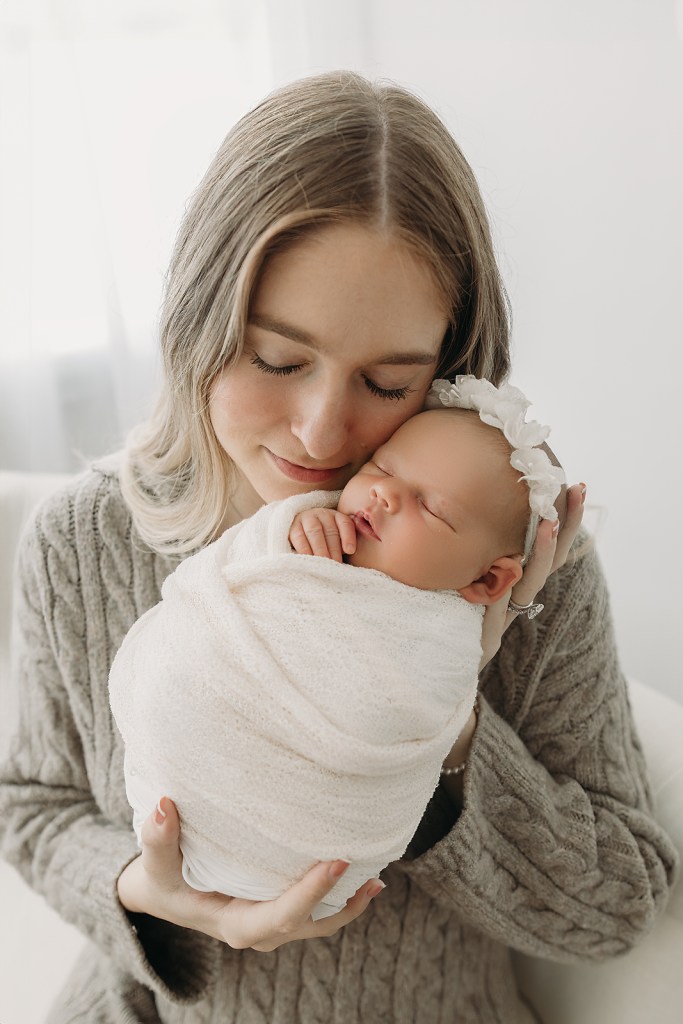 Mother holds newborn baby girl with gentle affection during newborn photos in Tampa