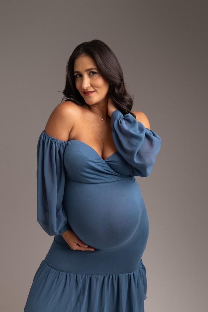 Pregnant mother wearing blue dress tenderly cradles her pregnant stomach for maternity photoshoot Tampa