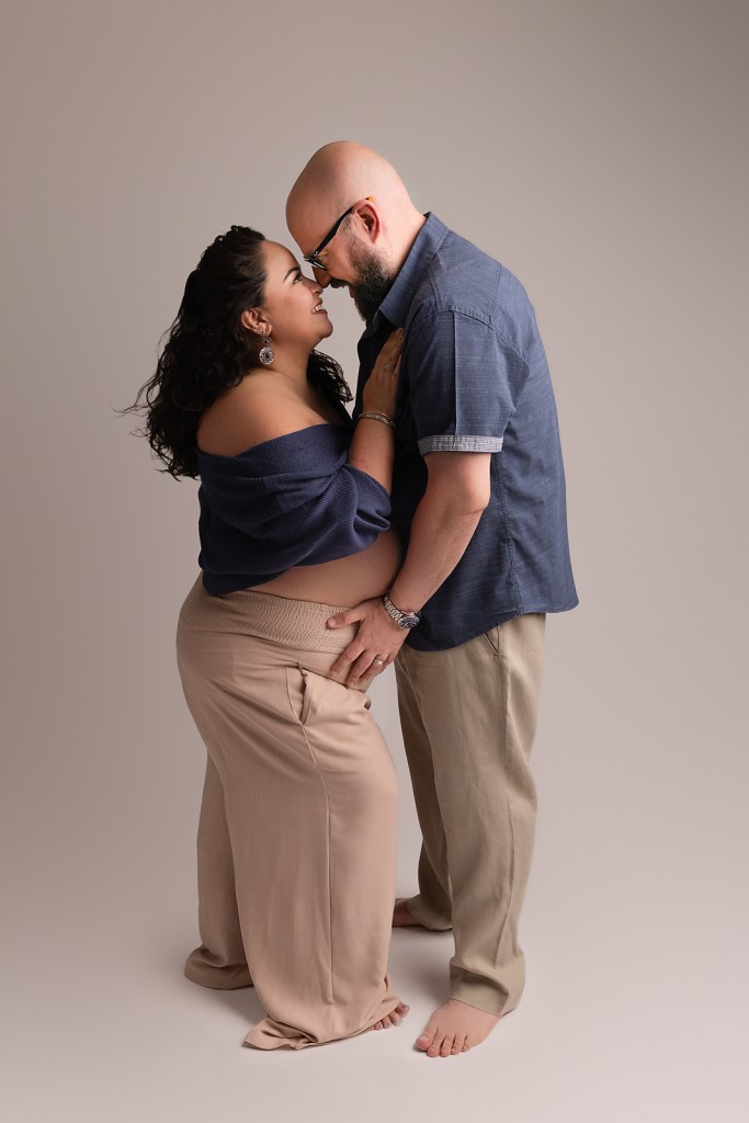 Pregnant couple smiling at each other while wearing casual clothes 