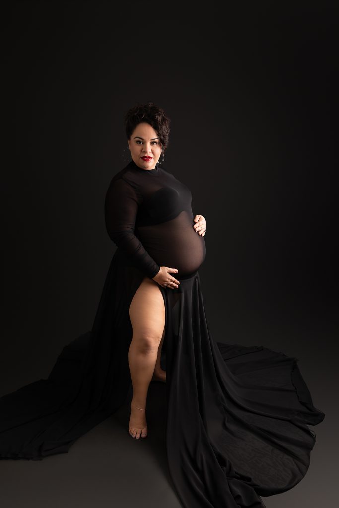 Artistic maternity portrait in black dress against dark background with flowing fabric and moody lighting for maternity photographer tampa