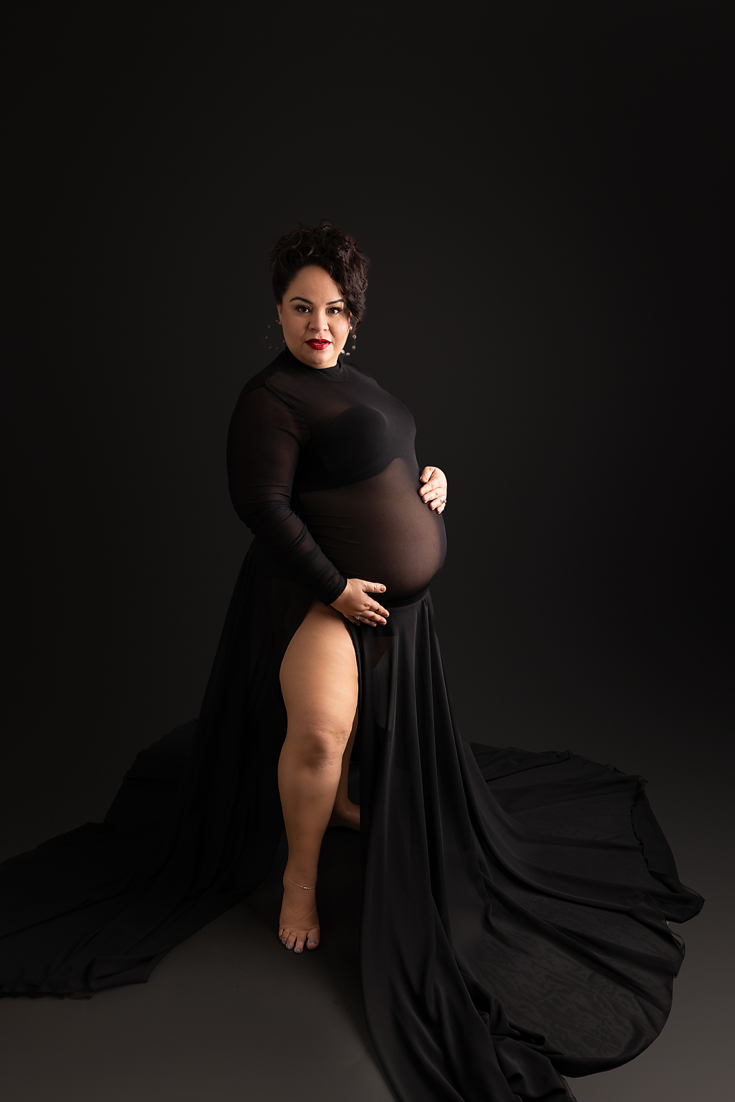 Artistic maternity portrait in black dress against dark background with flowing fabric and moody lighting for Tampa maternity photographer
