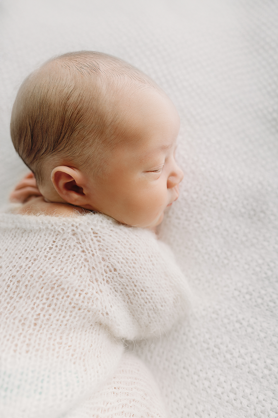 Close-up profile of sleeping newborn baby wrapped in soft white knit blanket during Tampa newborn photography session