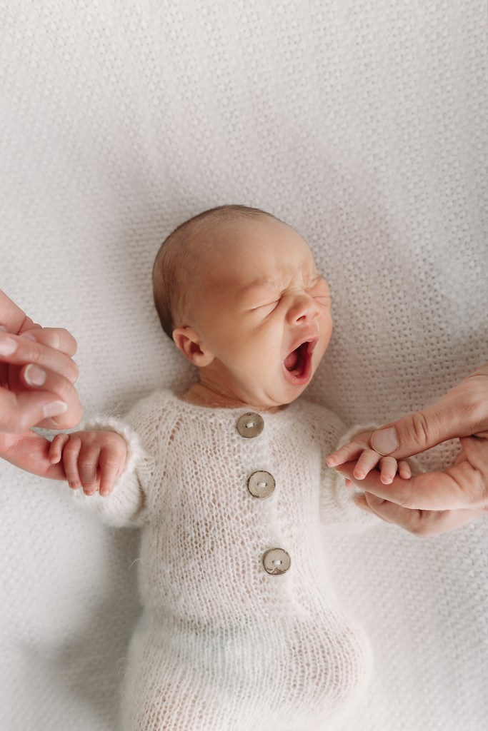 newborn baby boy in white knit romper yawns during tampa newborn photography session