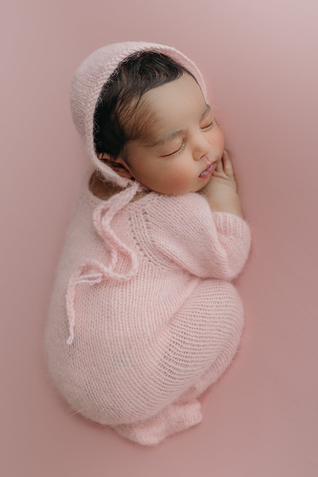 Sleeping newborn baby wrapped in soft pink knitted blanket on pink backdrop for newborn photography Tampa