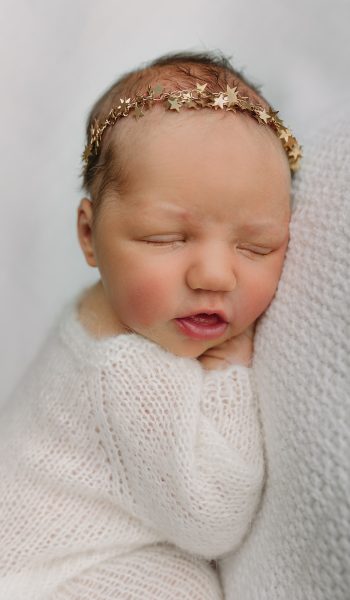 A sleeping newborn wrapped in a soft white knit blanket
