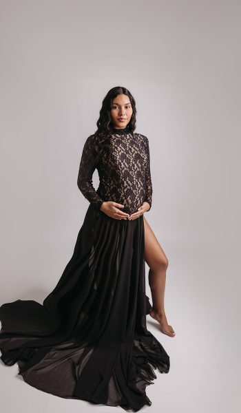 Ethereal maternity portrait with flowing champagne dress against dark backdrop.