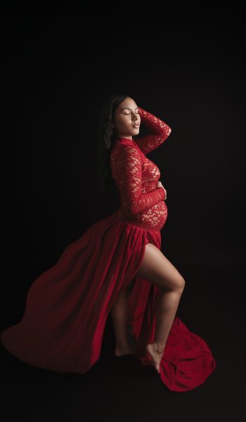 A dramatic maternity photographer Tampa session featuring a flowing red lace gown against a dark background.