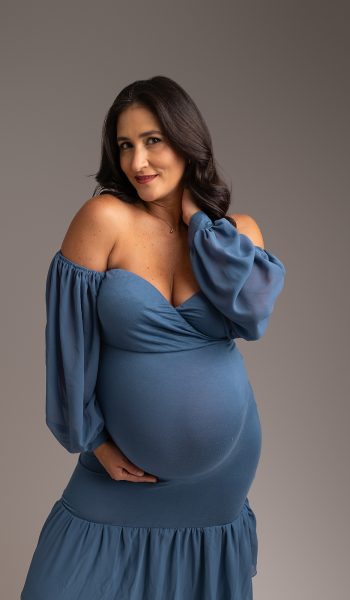 Pregnant mother wearing blue dress tenderly cradles her pregnant stomach for maternity photoshoot Tampa