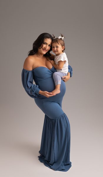 Maternity portrait in Tampa showing a tender moment between parent and child, wearing white shirts and denim against a grey backdrop.