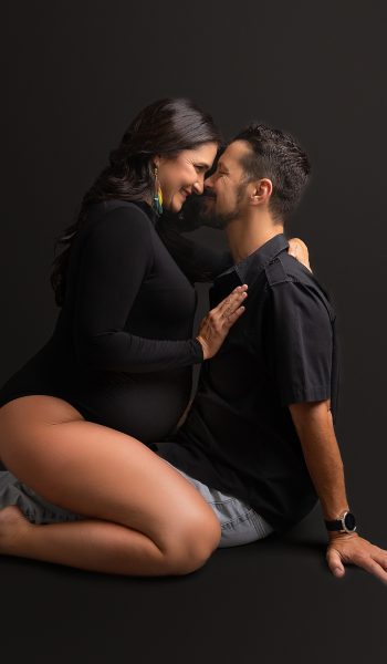 Intimate pregnancy photo series in Tampa showing two people embracing in dark, artistic studio lighting.