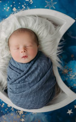 baby boy wrapped in blue swaddle with moons and stars background during tampa newborn photos