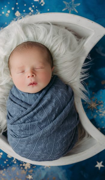 baby boy wrapped in blue swaddle with moons and stars background during tampa newborn photos