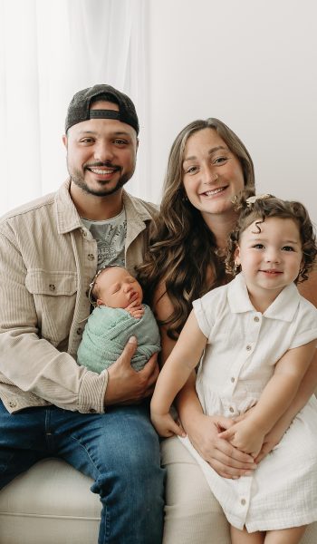 father holds little girl and newborn baby while smiling at the camera