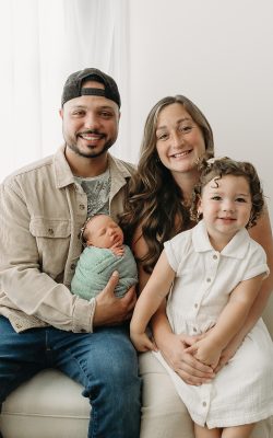 father holds little girl and newborn baby while smiling at the camera
