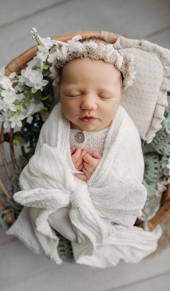 newborn baby girl swaddled in white bow and flowers