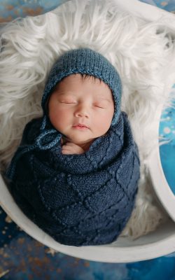 newborn swaddled in blue in a white moon prop on stars and moons background