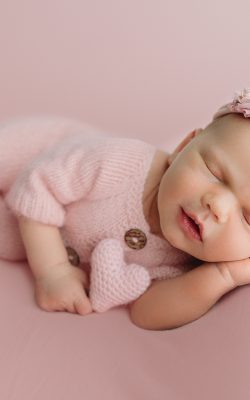 newborn baby girl poses in side laying pose on pink blanket