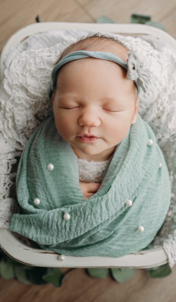 baby girl swaddled in sage green poses for newborn photos