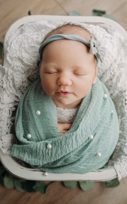 baby girl swaddled in sage green poses for newborn photos